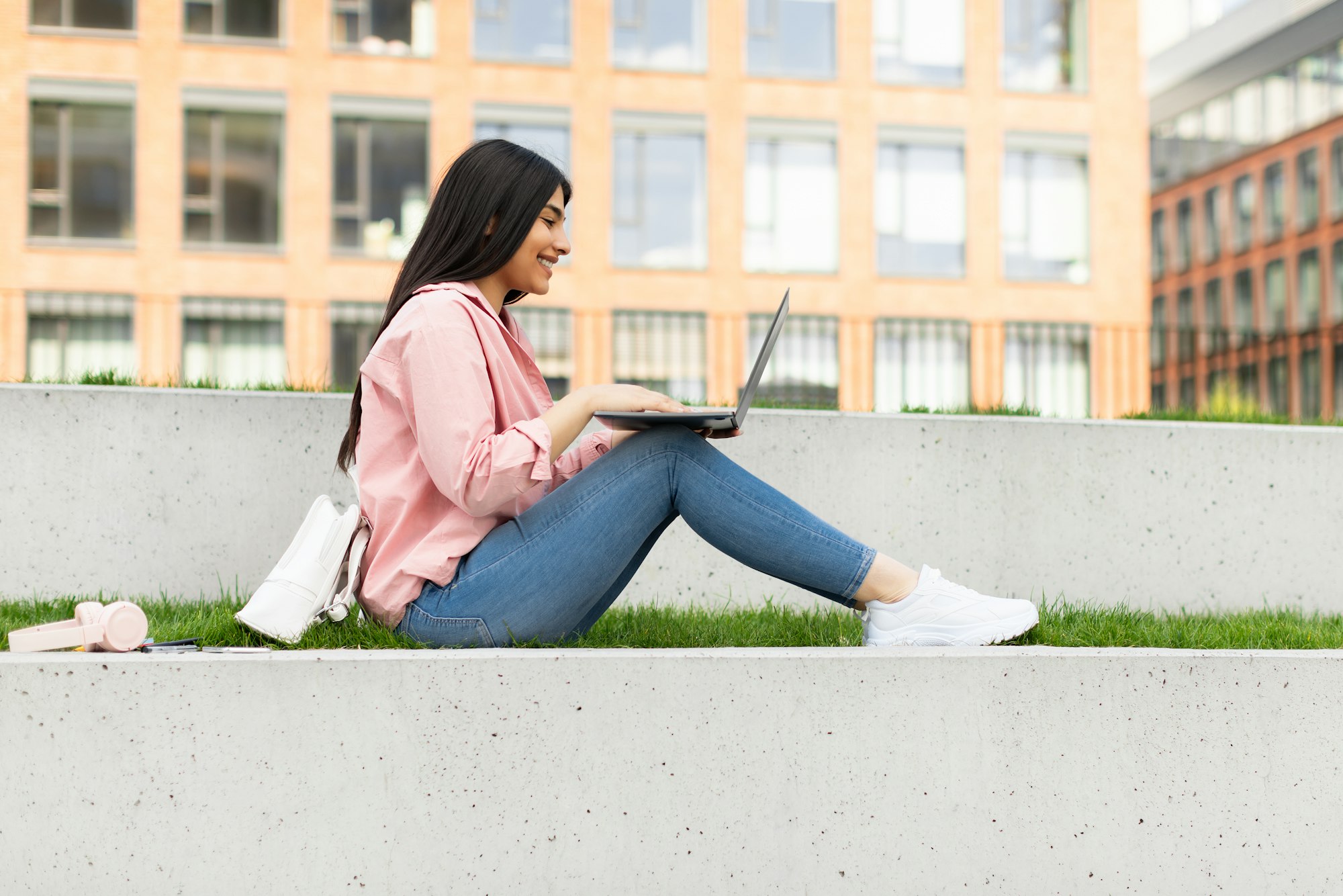 Teen lady using laptop outdoors, studying online, sitting in college campus and preparing for exams